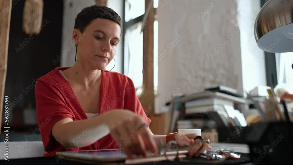 Tired woman architect with short hair in eyeglasses working on tablet and drinking coffee in the office Tired woman architect with short hair in eyeglasses working on tablet and drinking coffee in the office