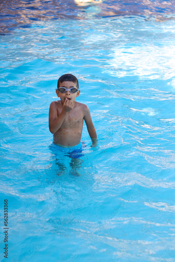 Young boy kid child six years old splashing in swimming pool having fun leisure activity wearing sea glasses practicing swimming