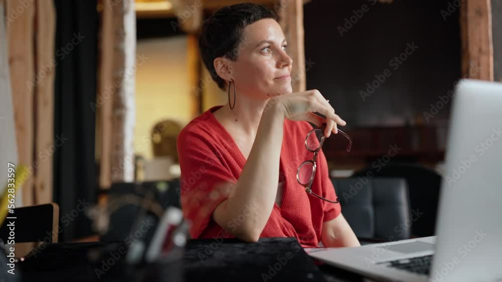 Cute brunette woman architect in eyeglasses working on laptop and looking at the camera in the office Cute brunette woman architect in eyeglasses working on laptop and looking at the camera in the office