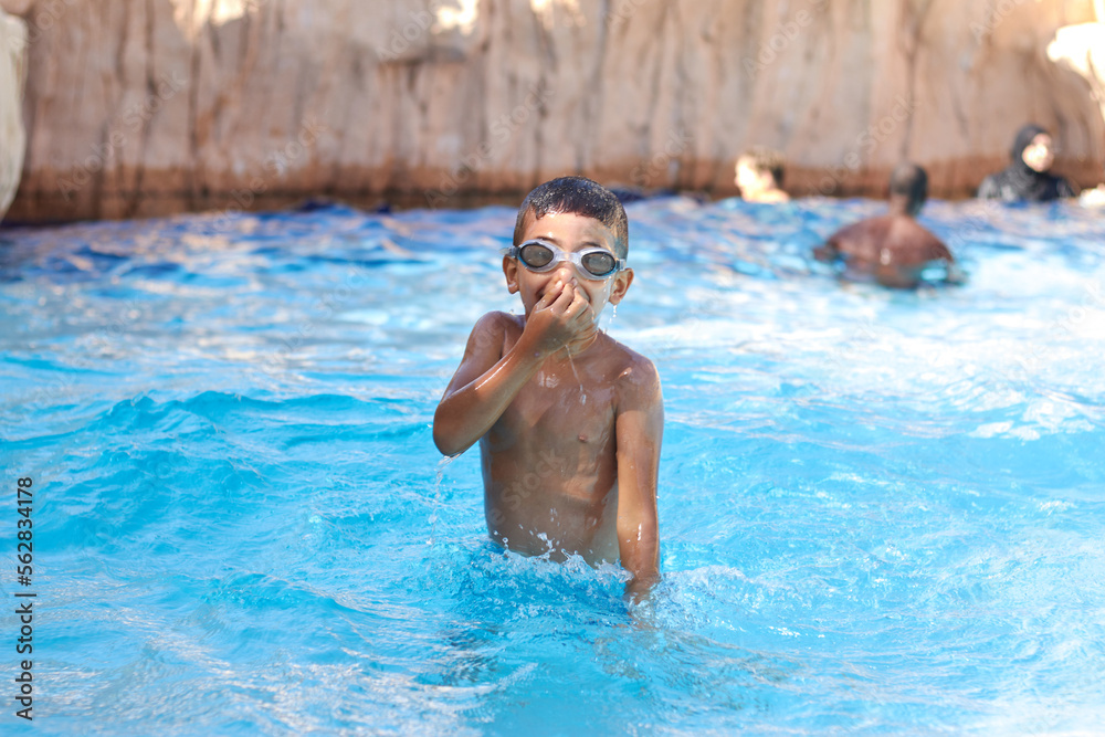 Young boy kid child six years old splashing in swimming pool having fun leisure activity wearing sea glasses practicing swimming