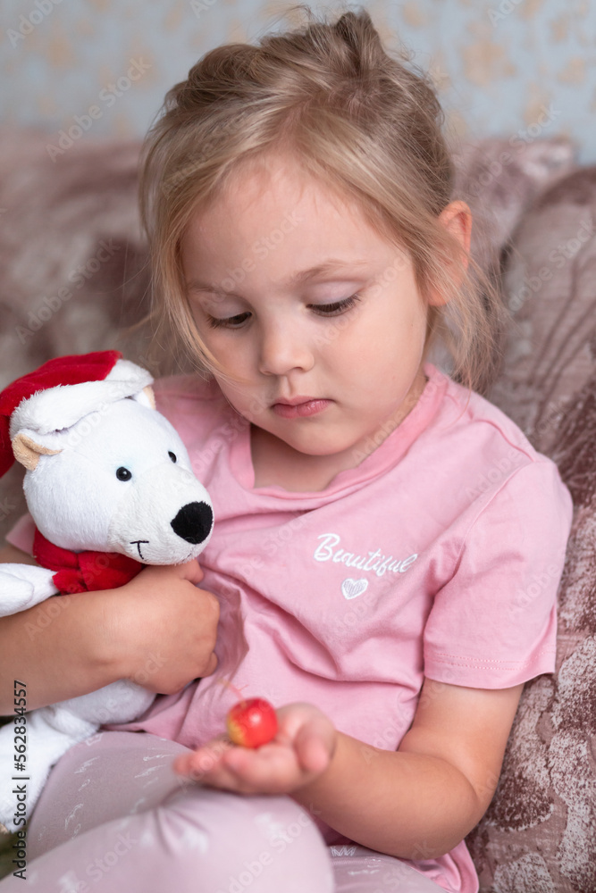 A girl of four years old sits with her inrushka, a white bear and an apple close-up. Vertical orientation. A girl of four years old sits with her inrushka, a white bear and an apple close-up. Vertical orientation.