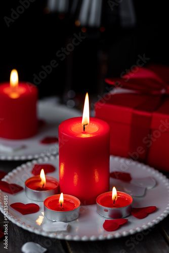 Saint Valentine's Day celebration. Red burning candles, hearts, gift box, postcard on dark wooden background. Happy holiday . Table decor for festive dinner, romantic atmosphere
