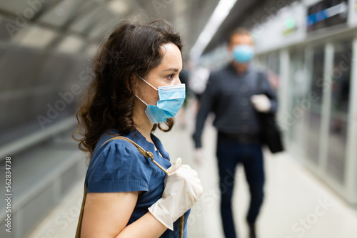 Personal protection during a pandemic. Woman in protective medical mask and gloves is standing on platform and waiting train