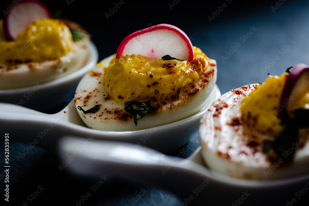 Deviled eggs garnished with smoked paprika , sliced radish , and chopped basil.
