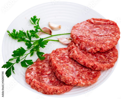 Shaped patties for burgers from raw ground beef meat with fresh parsley sprigs, spicy garlic and allspice on plate. Isolated over white background