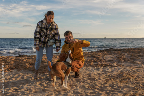 Loving couple is playing with their dog at the beach - caucasian people - people, animal, lifestyle and nature concept