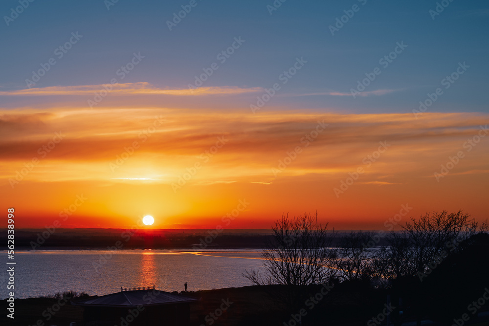 A beautiful sunset over Pegwell Bay. A person can be seen in silhouette watching the scene. The golden light is reflected in the water. A beautiful sunset over Pegwell Bay. A person can be seen in silhouette watching the scene. The golden light is reflected in the water.