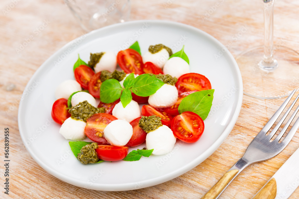 Caprese salad, sliced fresh mozzarella and tomatoes, served with basil leaves and pesto sauce.