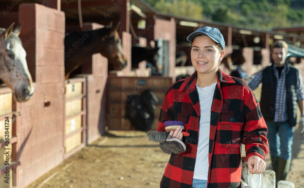 Portrait of young woman with brushes in her hands for cleaning and caring for horses at a horse farm