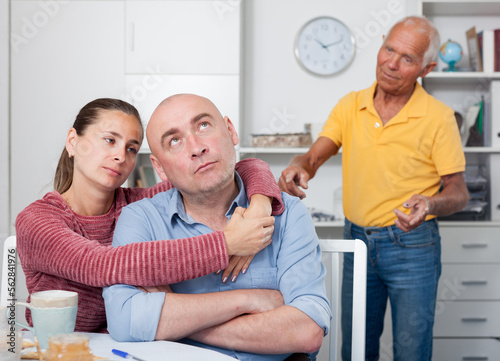 Unhappy family couple hugging after conflict, worried elderly man on backgroud © JackF