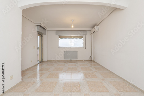 Living room of an empty house with aluminum windows with a radiator below and exit to a terrace with a glass door