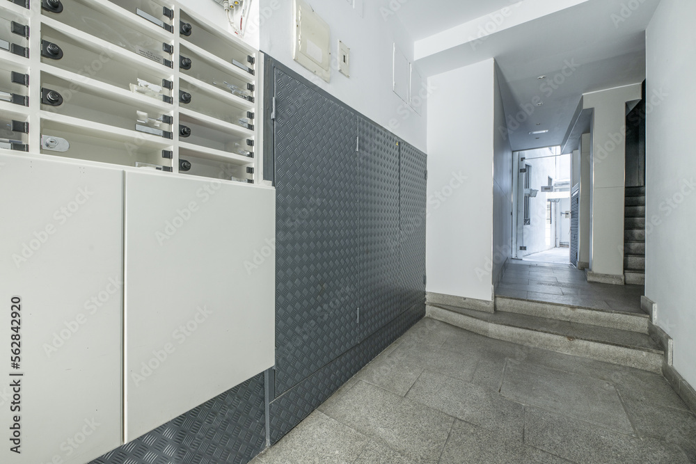 Access portal to a building with granite tiles on the stairs to access an elevator with gray doors and wrought iron railing and methacrylate letterboxes Access portal to a building with granite tiles on the stairs to access an elevator with gray doors and wrought iron railing and methacrylate letterboxes