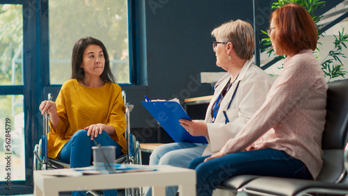 Фотография Asian woman with chronic impairment doing consultation with physician in clinic lobby, giving healthcare advice for disability and health condition
