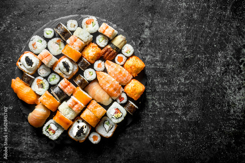 Set of different kinds of sushi rolls on a round stone Board.