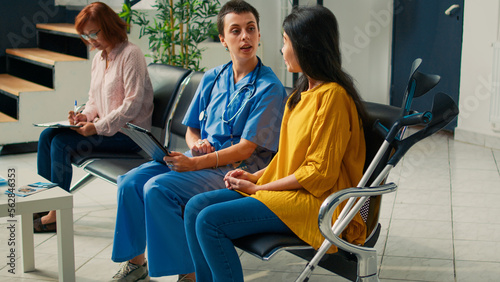 Bilde på lerret Medical assistant consulting asian woman with crutches, using digital tablet to fill in checkup report and receive healthcare insurance