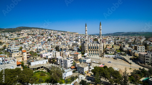 Aerial view flying over an arab cityscape buildings and streets, with view of a beautiful mosque with two turrets and golden dome