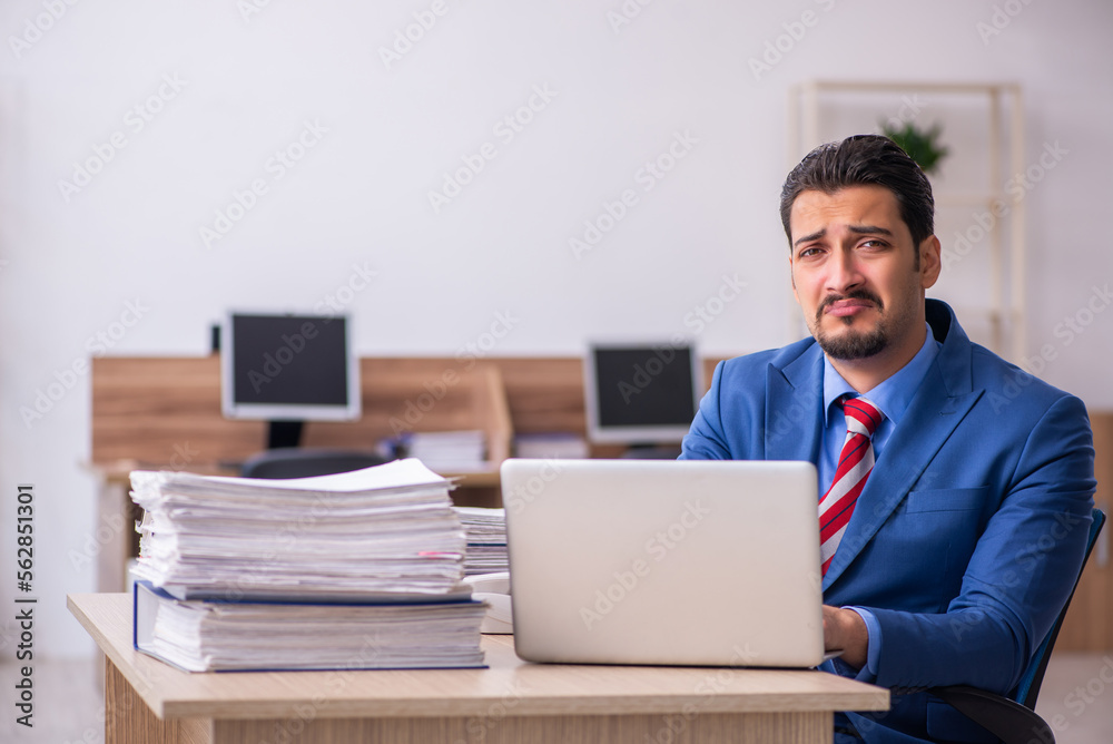 Young male employee unhappy with excessive work at workplace Young male employee unhappy with excessive work at workplace