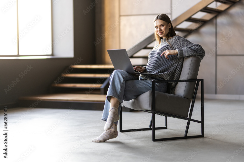 Happy woman holding laptop while sitting on a chair over gray background Happy woman holding laptop while sitting on a chair over gray background