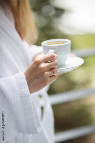 Girl in a white bathrobe with a cup of hot tea on the balcony. Hands and cup close-up.