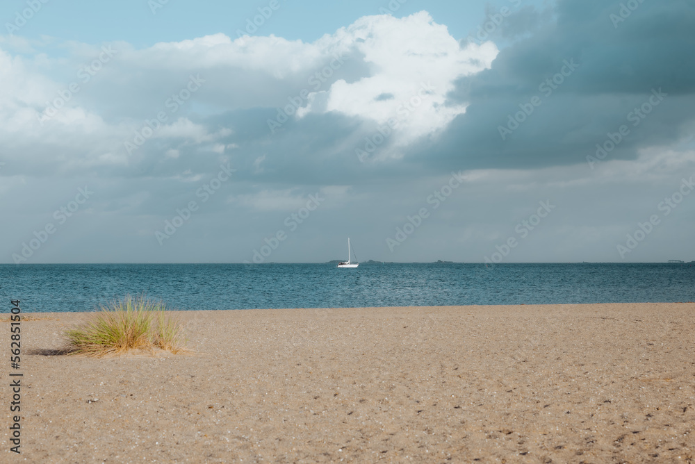 Horizontal view of a sailing boat in front of a beach with a blue sky in Amager beach, Copenhagen