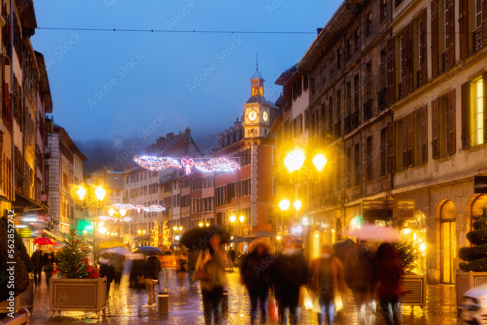 Fototapeta premium Night view of Place Saint-Leger, pedestrian street in historic center of French city of Chambery decorated with traditional Christmas lights overlooking main clock tower.