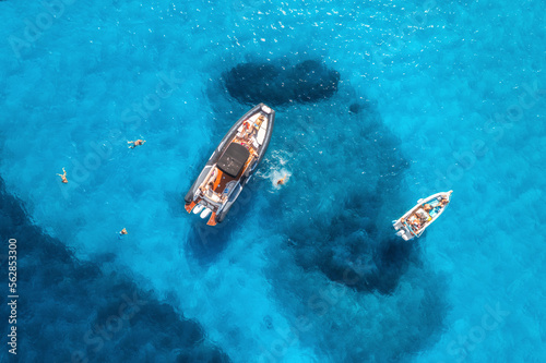 Aerial view of yachts and swimming people in blue sea at sunset in summer. Sardinia, Italy. View from above of speed boats, yachts, transparent water. Top view from drone. Tropical seascape. Vacation