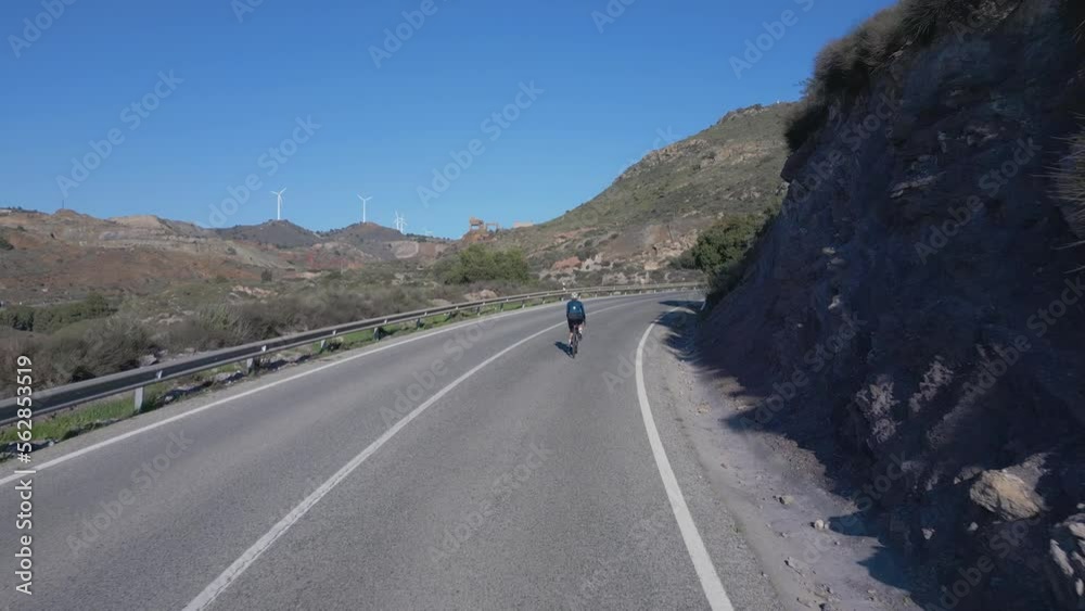 Camera follows female road cyclist during her training in mountains. Cardio training pushing pedals hard on uphill. Pursuing your cycling dreams. Female athlete trains for the race. Cartagena, Spain Camera follows female road cyclist during her training in mountains. Cardio training pushing pedals hard on uphill. Pursuing your cycling dreams. Female athlete trains for the race. Cartagena, Spain