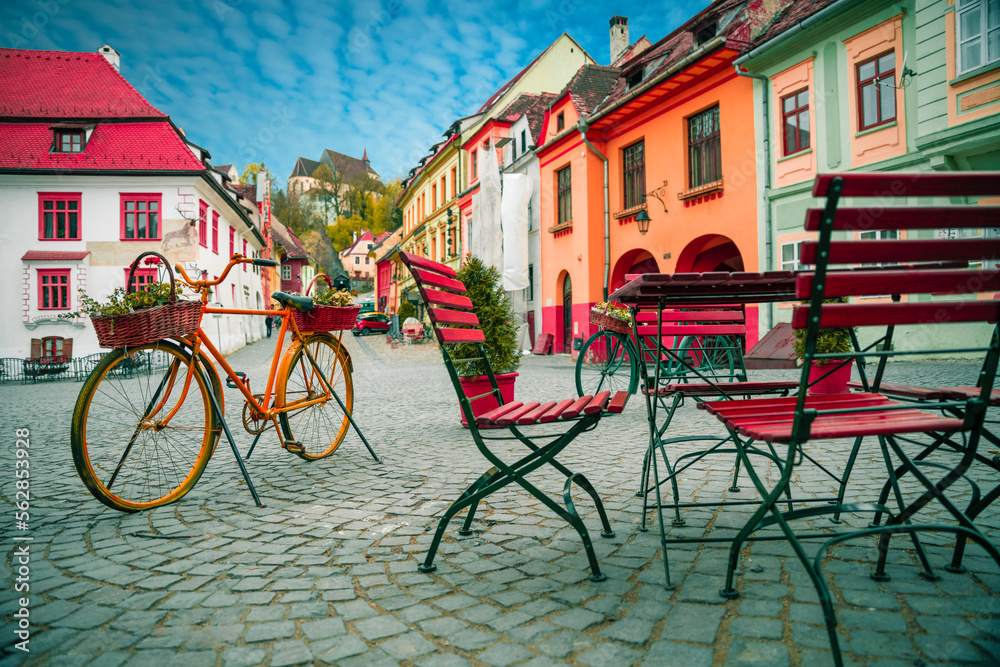 Decorative bicycle next to cafe bar with Stone paved old street and colorful buildings in city center, Sighisoara, Transylvania, Romania, Europe