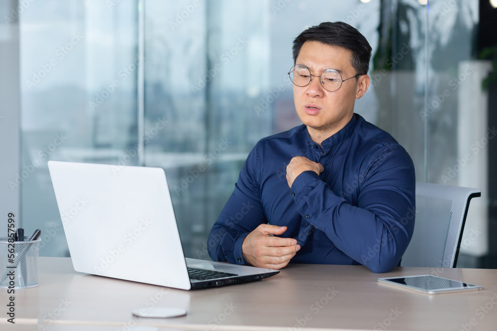 Heat and heat in the office, broken air conditioner, Asian man has nothing to breathe, businessman lacks fresh air, man works inside the office wearing glasses and using a laptop at work. Heat and heat in the office, broken air conditioner, Asian man has nothing to breathe, businessman lacks fresh air, man works inside the office wearing glasses and using a laptop at work.