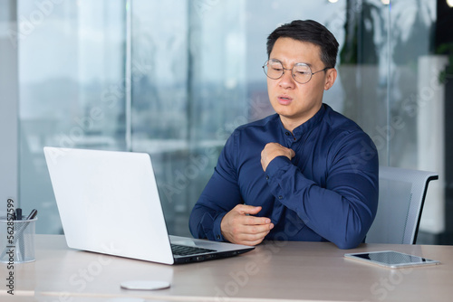 Heat and heat in the office, broken air conditioner, Asian man has nothing to breathe, businessman lacks fresh air, man works inside the office wearing glasses and using a laptop at work.