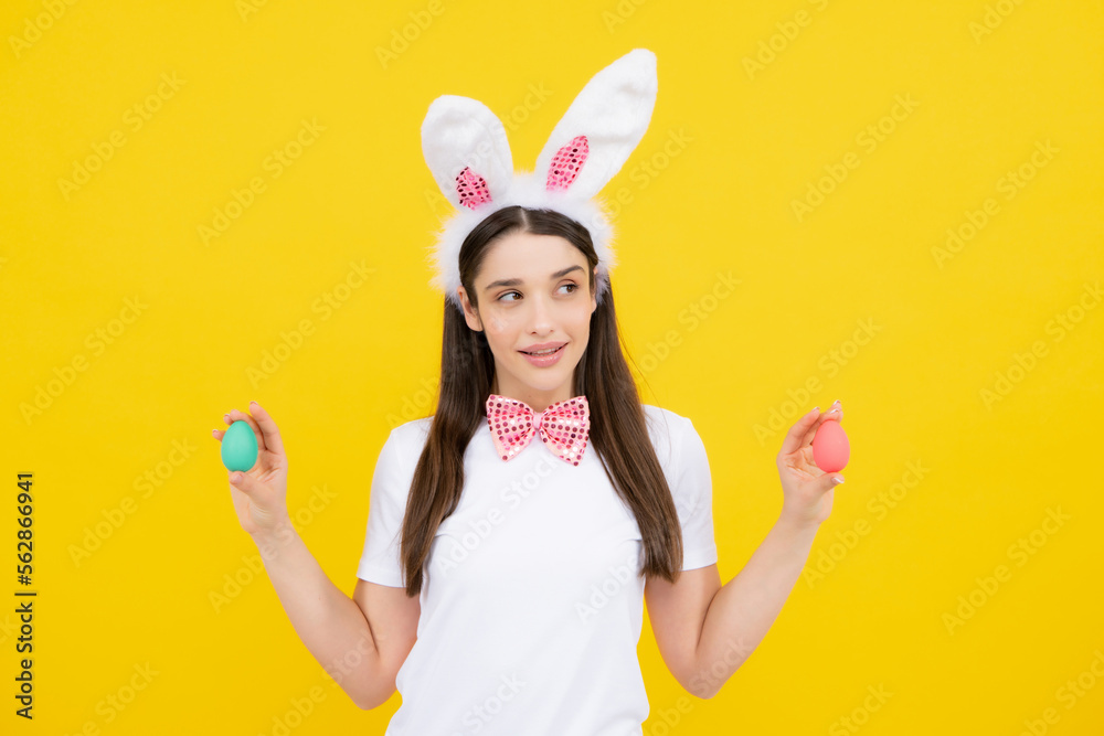 Happy Easter. Portrait of young smiling woman with bunny ears isolated on yellow studio background. Easter bunny woman looks fun. Easter eggs.