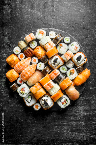 Set of different kinds of sushi rolls on a round stone Board.