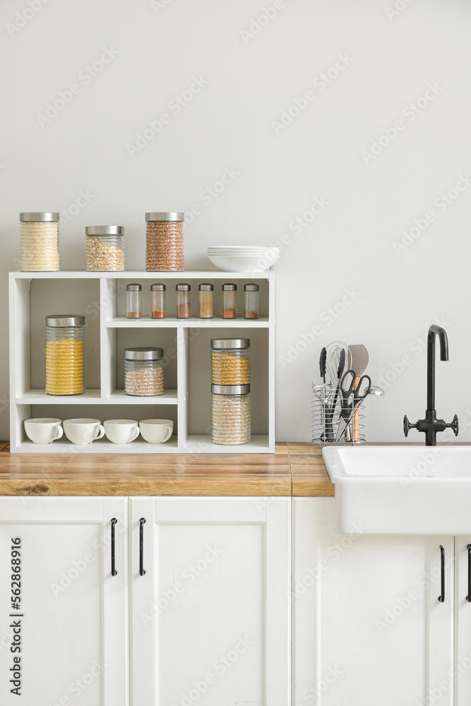 Jars with cereals, spices and utensils on kitchen counter