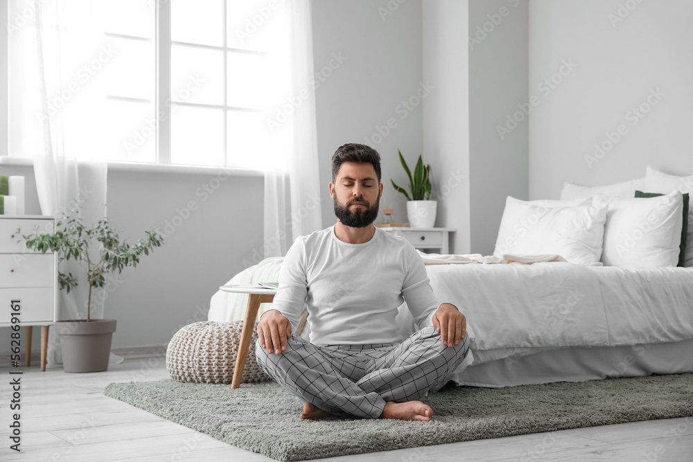 Handsome young man meditating on carpet at home Handsome young man meditating on carpet at home