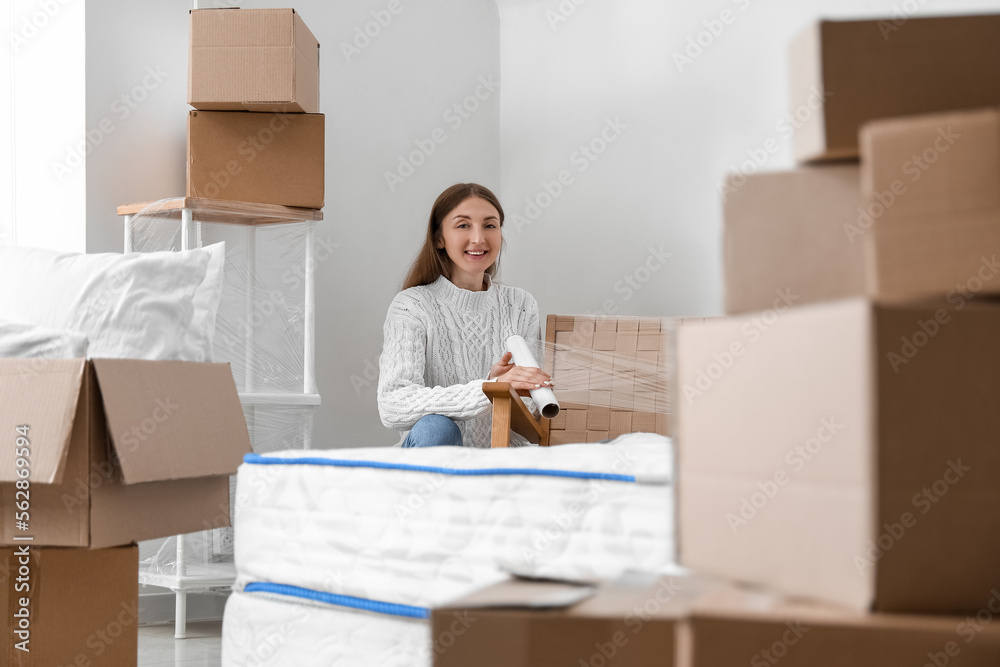 Young woman wrapping armchair in bedroom on moving day Young woman wrapping armchair in bedroom on moving day