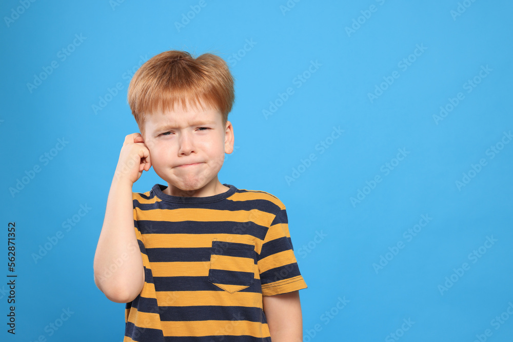 Little boy suffering from ear pain on light blue background. Space for text