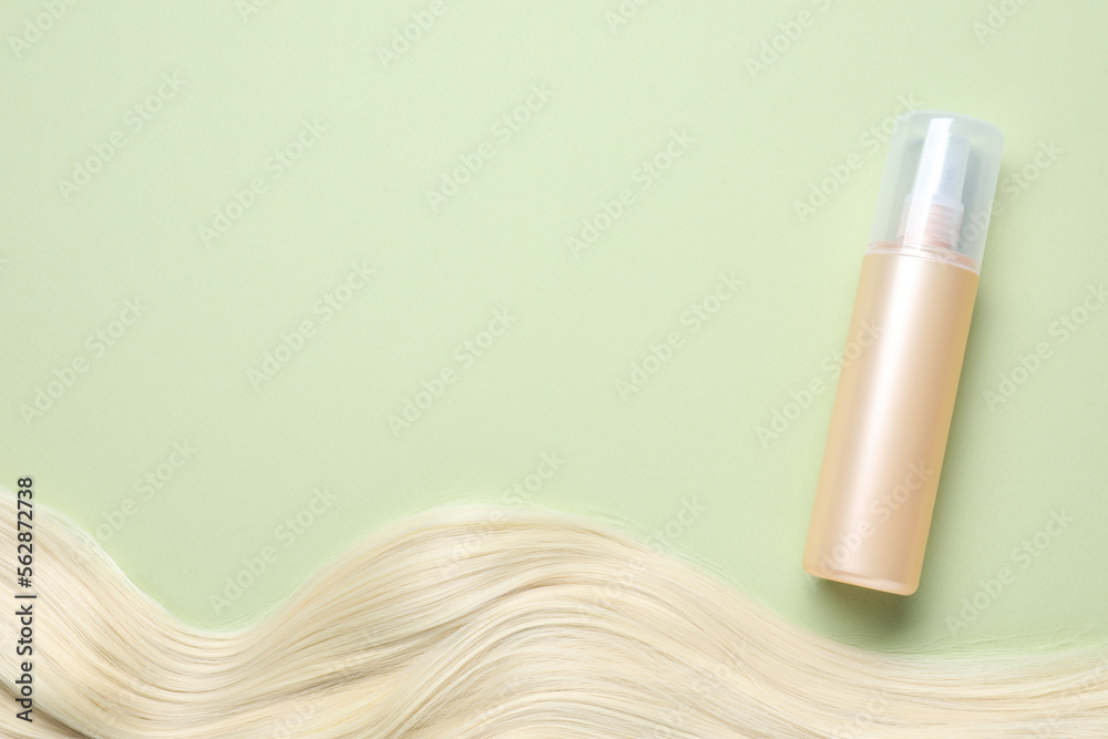 Fototapeta premium Spray bottle with thermal protection and lock of blonde hair on pale green background, flat lay. Space for text