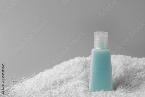 Winter skin care. Hand cream on artificial snow against light grey background, space for text