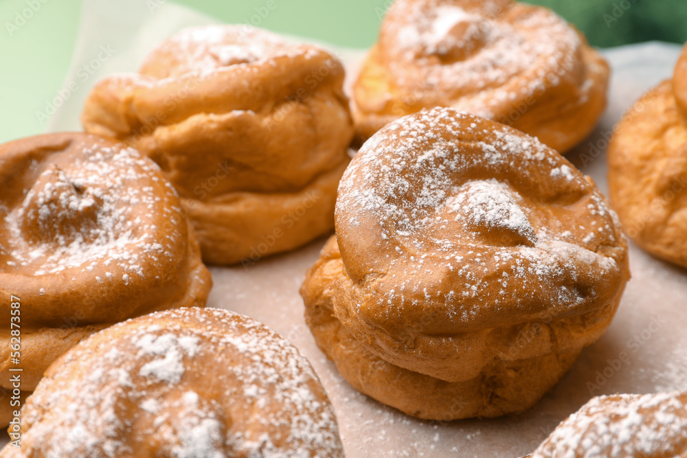 Delicious profiteroles with powdered sugar on parchment paper, closeup