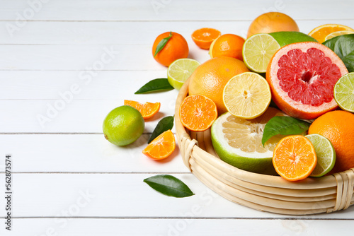 Different ripe citrus fruits with green leaves on white wooden table. Space for text