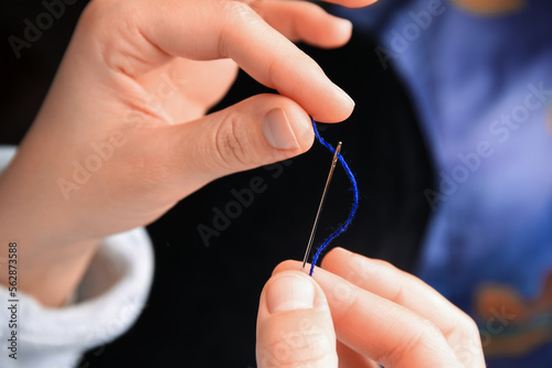 Woman threading sewing needle on blurred background  closeup