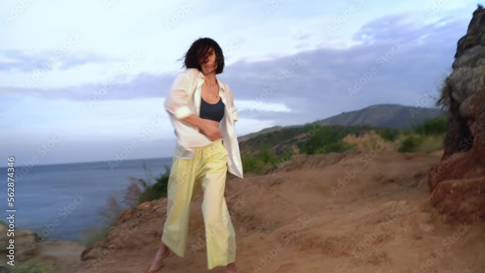 Modern jazz dance on mountain by sea performed by a young lady in wireless headphones in Thailand. Young adult caucasian woman is moving and feeling rhythm listening to music in wireless headphones Modern jazz dance on mountain by sea performed by a young lady in wireless headphones in Thailand. Young adult caucasian woman is moving and feeling rhythm listening to music in wireless headphones
