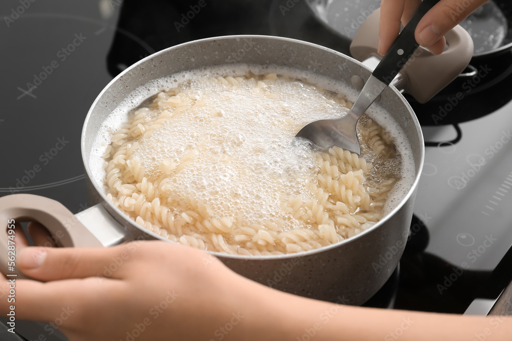 Woman cooking tasty pasta on stove, closeup