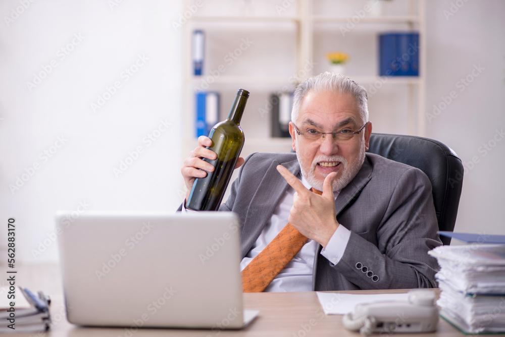 Old male employee drinking alcohol at workplace Old male employee drinking alcohol at workplace
