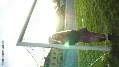 Blonde woman in skirt and lather jacket stands near soccer net at sport field