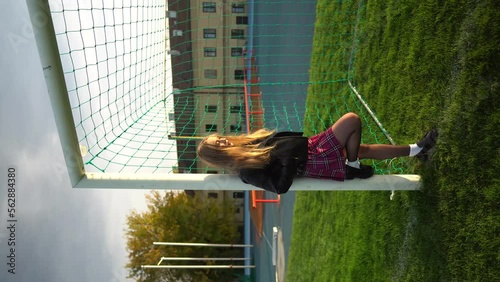 Blonde woman in skirt and lather jacket stands near soccer net at sport field