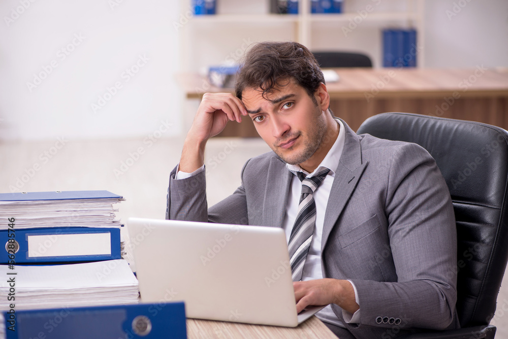 Young male employee unhappy with excessive work in the office Young male employee unhappy with excessive work in the office