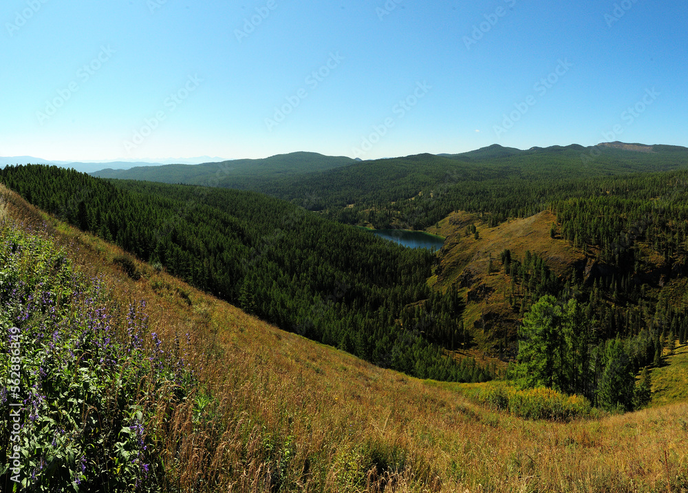 A small mountain lake in a lowland near high hills overgrown with coniferous forest.
