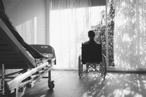 The woman sitting on wheelchair. She is see window with patient bed in hospital.disabled person lonely. Photo concept depression and Patient.