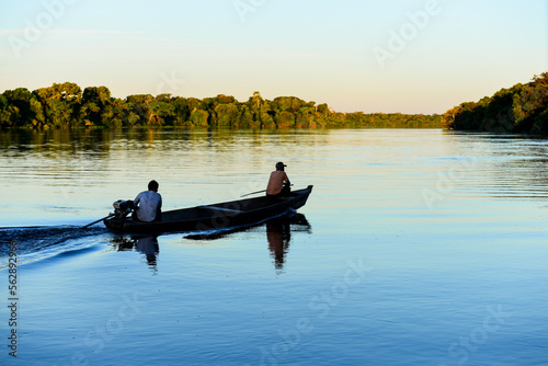 Two men on a boat at sunset on the rainforest-lined Guaporé-Itenez river, near the remote village of Mateguá, Beni Department, Bolivia, on the border with Rondonia, Brazil